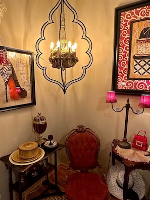 A room with a chandelier, a red chair, a small table with a lamp, and a framed picture on the wall.