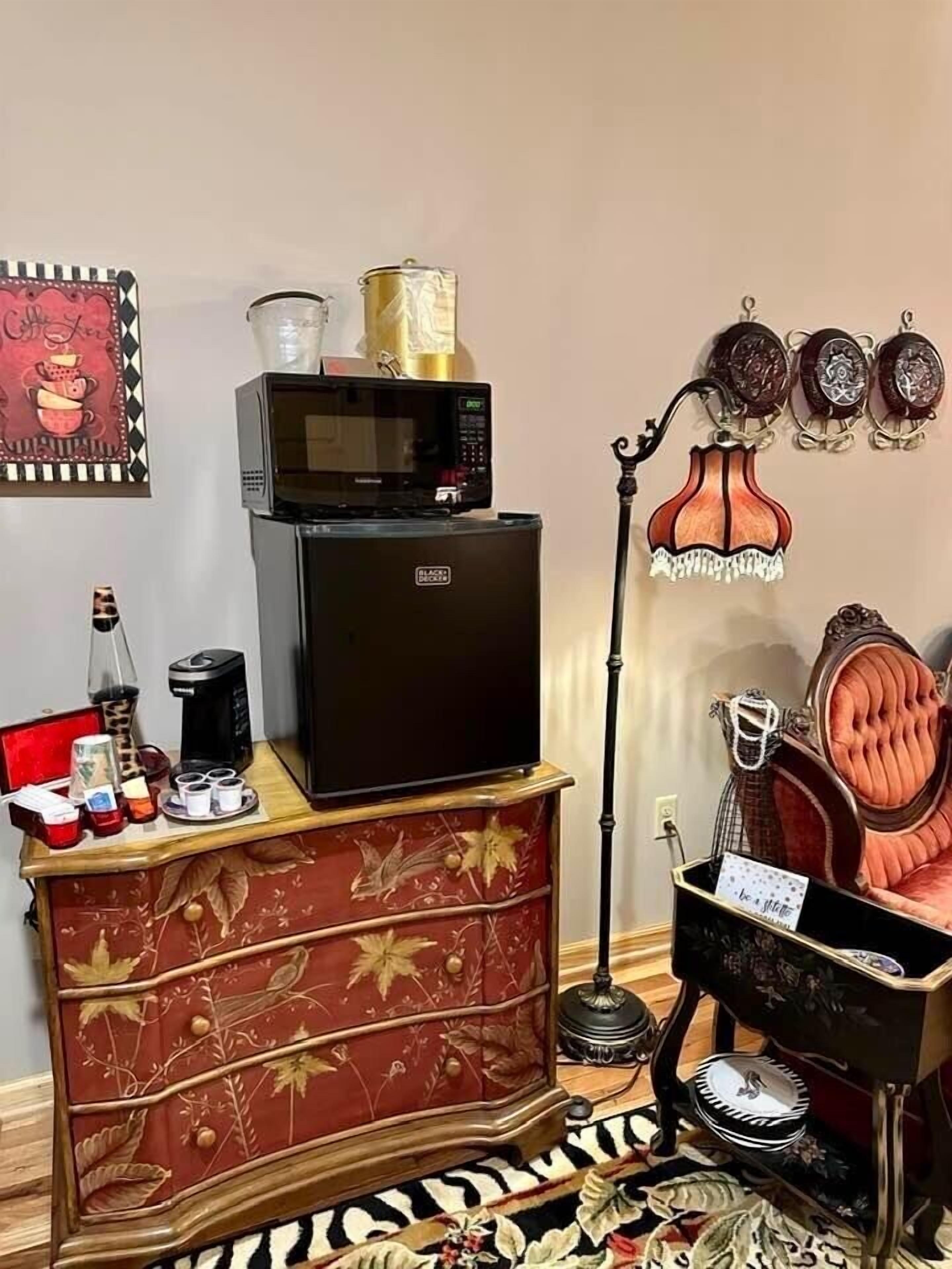 Ein Zimmer mit Minibar, einer Kaffeemaschine, einem Zierteil, einer Lampe und einem Bett mit Kopfteil.