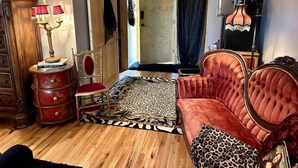 Une pièce avec un canapé en velours rouge, un tapis à motifs, un plancher en bois, un buffet rouge et une lampe à plusieurs abat-jour.