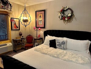 A bedroom with a large bed, a red chair, a small table, and a wall-mounted heater.