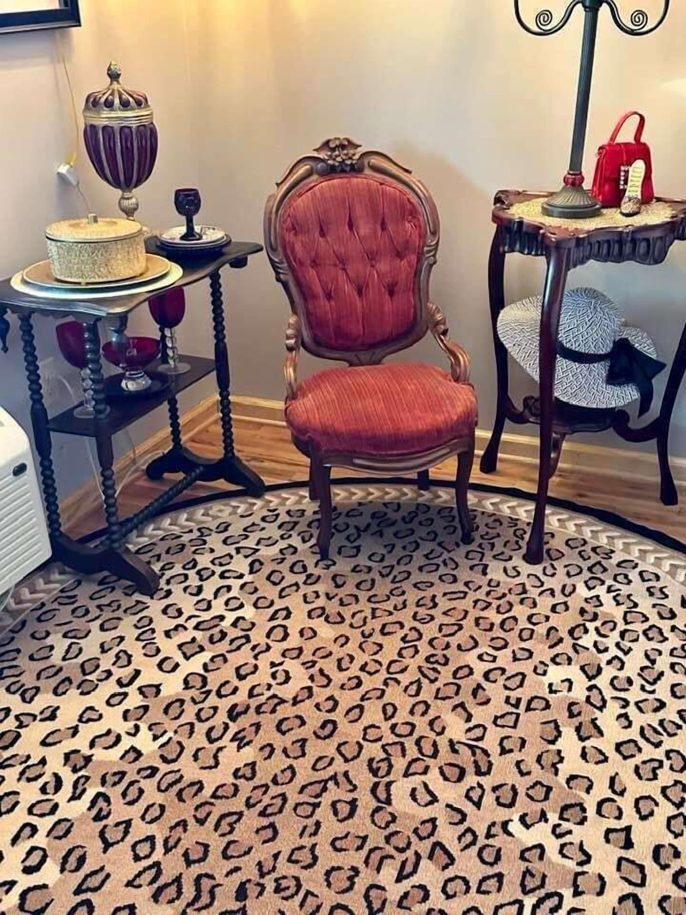 Una habitación con alfombra de estampado de leopardo, una butaca tapizada de rojo, una mesita con un bolso rojo y una lámpara decorativa.