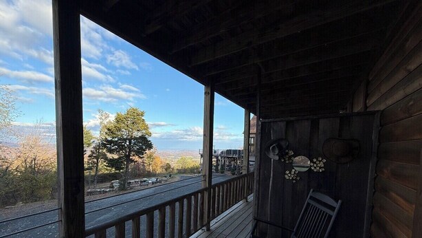 Une véranda en bois avec une balustrade, un fauteuil à bascule et une vue sur une route et des arbres.