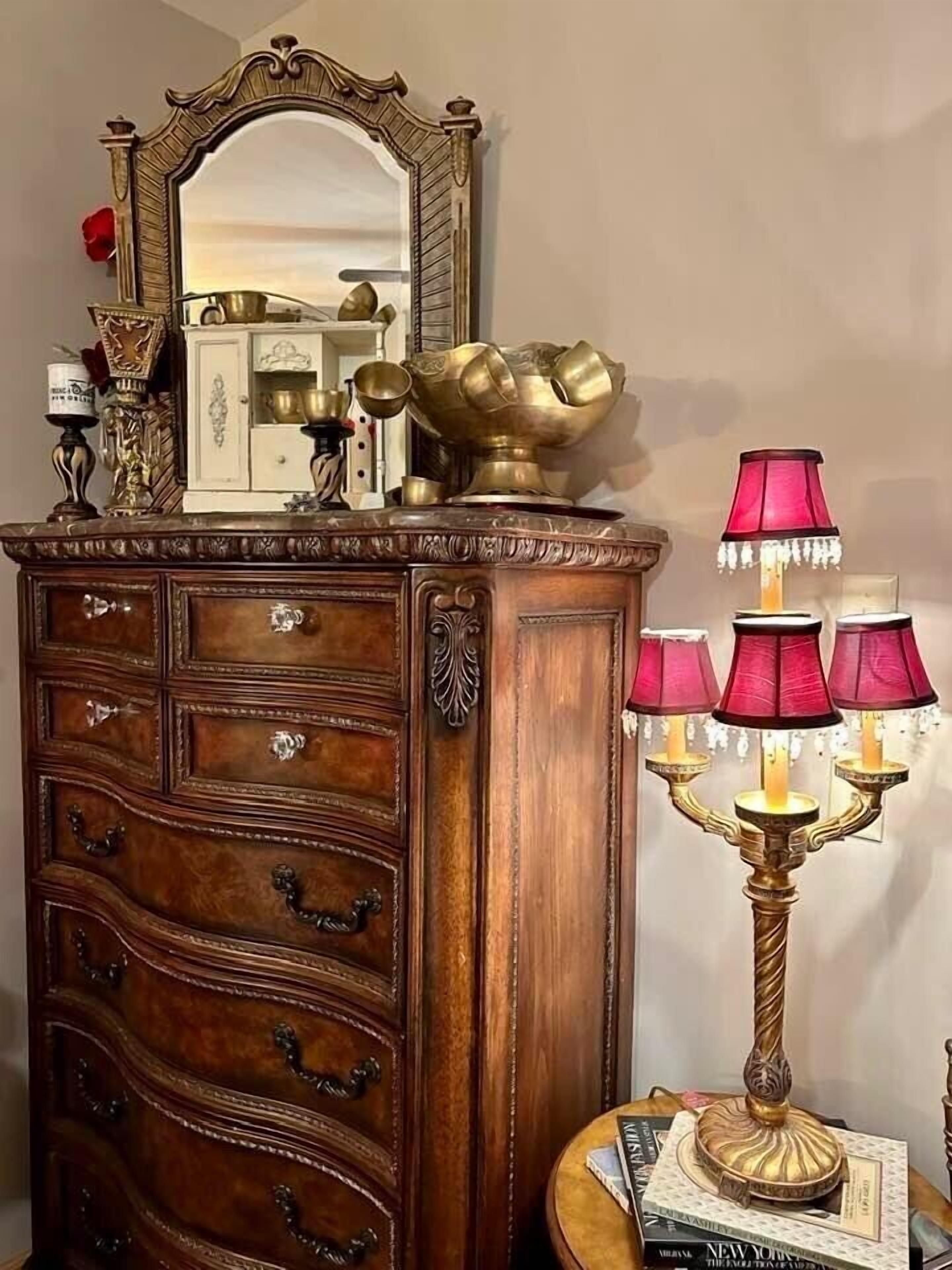 A wooden dresser with a mirror, brass decorative items, and a candelabra with pink lamps.