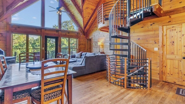 A wooden cabin interior with a dining area, a sofa, and a spiral staircase. - Cabin #10 - Our Mountain Cabin (Stanardsville)