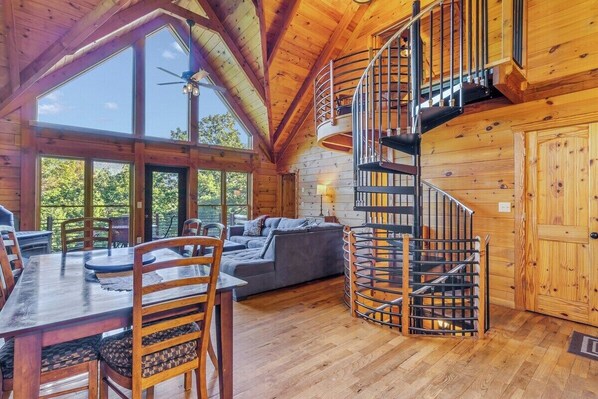 A wooden cabin interior with a dining area, a sofa, and a spiral staircase.