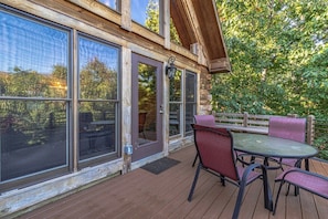 A wooden deck with a table and chairs, large windows, and a wooden fence.