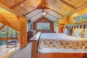 A wooden cabin with a loft bedroom, a desk, and a rocking chair.