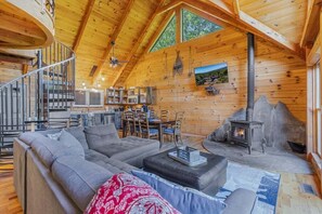 A log cabin interior with a living area, kitchen, and fireplace.