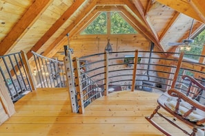 A wooden interior with a curved staircase, a rocking chair, and a view of greenery outside.