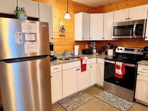 A kitchen with white cabinets, stainless steel appliances, and patterned rugs. - Speckled Owl Mountain Cabin (Stanardsville)