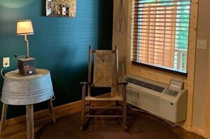 A room with a vintage radio on a metal bucket, a wooden chair, a window with blinds, and a wall-mounted heater. - Old Wash House - Rm. 104 (Stanardsville)