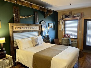 A bedroom with a bed, a wash bed company sign, a mirror, and a window with blinds.