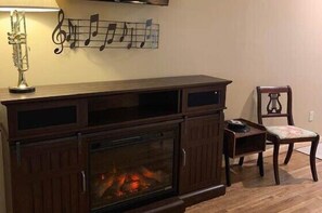 A living room with a fireplace, a music-themed wall decoration, a lamp, and a chair. - Music of the Mtns Rm. 203 (Stanardsville)