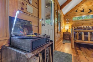 Interior de una cabaña de madera con un tocadiscos, paredes de madera, una puerta y una ventana.