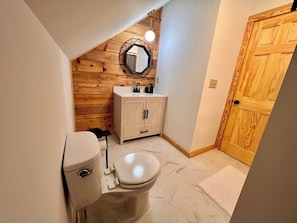 A compact bathroom with a wooden wall, a white toilet, a sink with a cabinet, and a round mirror.