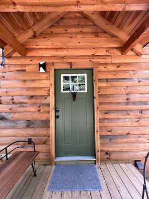 Une cabane en bois avec une porte verte, un banc et un petit espace de véranda.