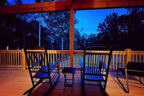 Une terrasse en bois, avec des chaises et un banc, donnant sur une étendue d’eau.