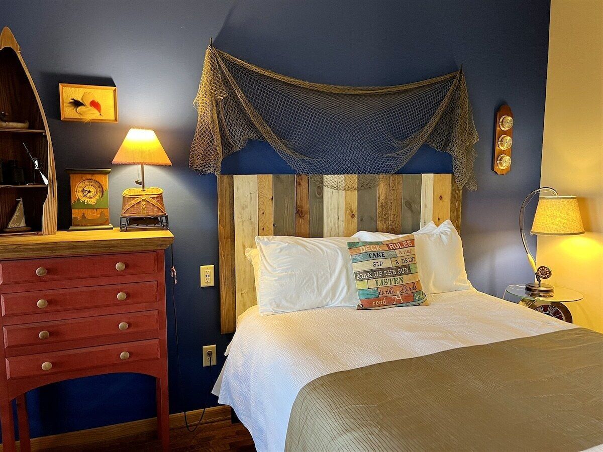 Een slaapkamer met een houten hoofdeinde, een bed met witte beddengoed, een nachtkastje met een lamp en een kledingkast met lades.