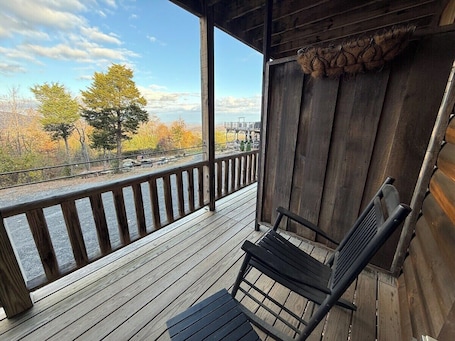 A wooden deck with a bench and railing, overlooking a scenic view of trees and a distant structure.. Farmer`s Market Rm. 102