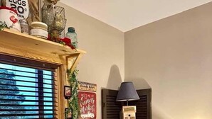 A corner room with a window, a radiator, a lamp, a small table, and decorative items. - Farmer`s Market Rm. 102 (Stanardsville)