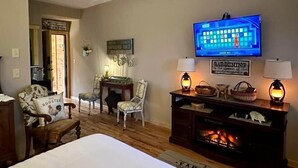 A room with a bed, a television, a fireplace, and two chairs. - Farmer`s Market Rm. 102 (Stanardsville)