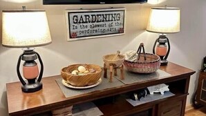 A living room with a fireplace, a television mounted on the wall, and two lamps on either side of a wooden console table. - Farmer`s Market Rm. 102 (Stanardsville)