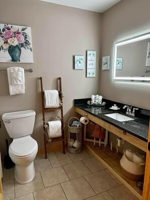 Ein Badezimmer mit Toilette, einem hölzernen Handtuchhalter, einem Waschbecken inklusive Spiegel und einer gerahmten Blumenblume an der Wand.