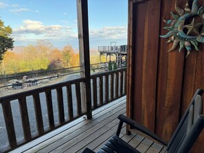 A wooden deck with a view of a river and a bridge, a rustic wall with a decorative sun, and a bench.