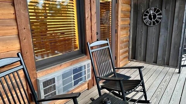 A wooden cabin with a porch, a clock, and a window with blinds. - Once Upon A Time Rm. 103 (Stanardsville)