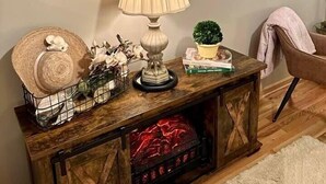 A living room with a flat-screen TV, a lamp, a small potted plant, a decorative basket, and a fireplace. - Once Upon A Time Rm. 103 (Stanardsville)