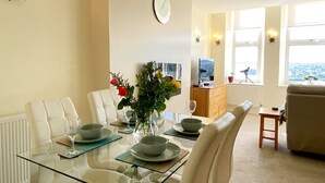 A dining area with a glass table, white chairs, a vase with flowers, and a clock on the wall. - Two Bed Apartment with a Millionaire's sea view (Torquay)