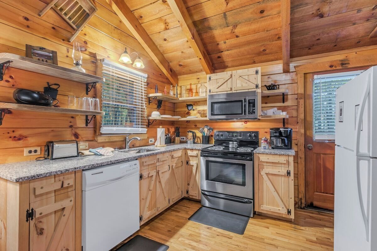 Una cocina tipo cabaña de madera con estufa, microondas y lavavajillas blanco.