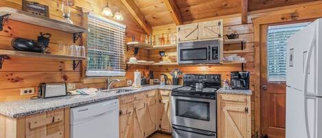 Una cocina tipo cabaña de madera con estufa, microondas y lavavajillas blanco.