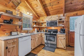 Una cocina tipo cabaña de madera con estufa, microondas y lavavajillas blanco.