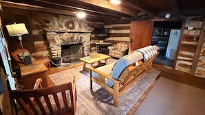 Interior acolhedor de uma cabana de madeira com lareira de pedra, móveis de madeira e um ambiente rústico.