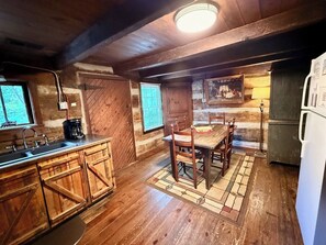 A rustic kitchen with wooden cabinets, a dining table, and a refrigerator.