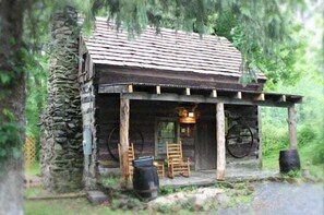 A rustic cabin with a porch, wooden chairs, and a wheel.