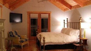 Ein Schlafzimmer mit Holzboden, einem Bett, einem Sessel, einem Fernseher und einer Tür.