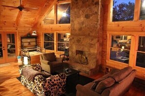 L’intérieur d’une cabane en rondins, avec une cheminée, des meubles en bois et de grandes fenêtres.