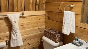 A wooden cabin bathroom with a toilet, sink, and towel rack. - Monarch Meadows Cabin Pod (Stanardsville)