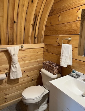 A wooden cabin bathroom with a toilet, sink, and towel rack.