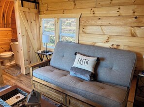 L’intérieur d’un chalet en bois, avec un canapé, une fenêtre et une porte en bois.