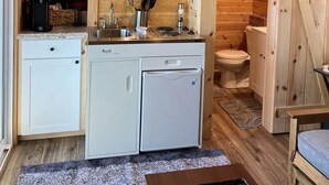 A compact kitchen with a microwave, sink, and white cabinets. - Monarch Meadows Cabin Pod (Stanardsville)