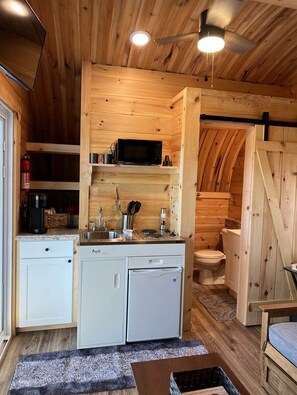 A compact kitchen with a microwave, sink, and white cabinets.