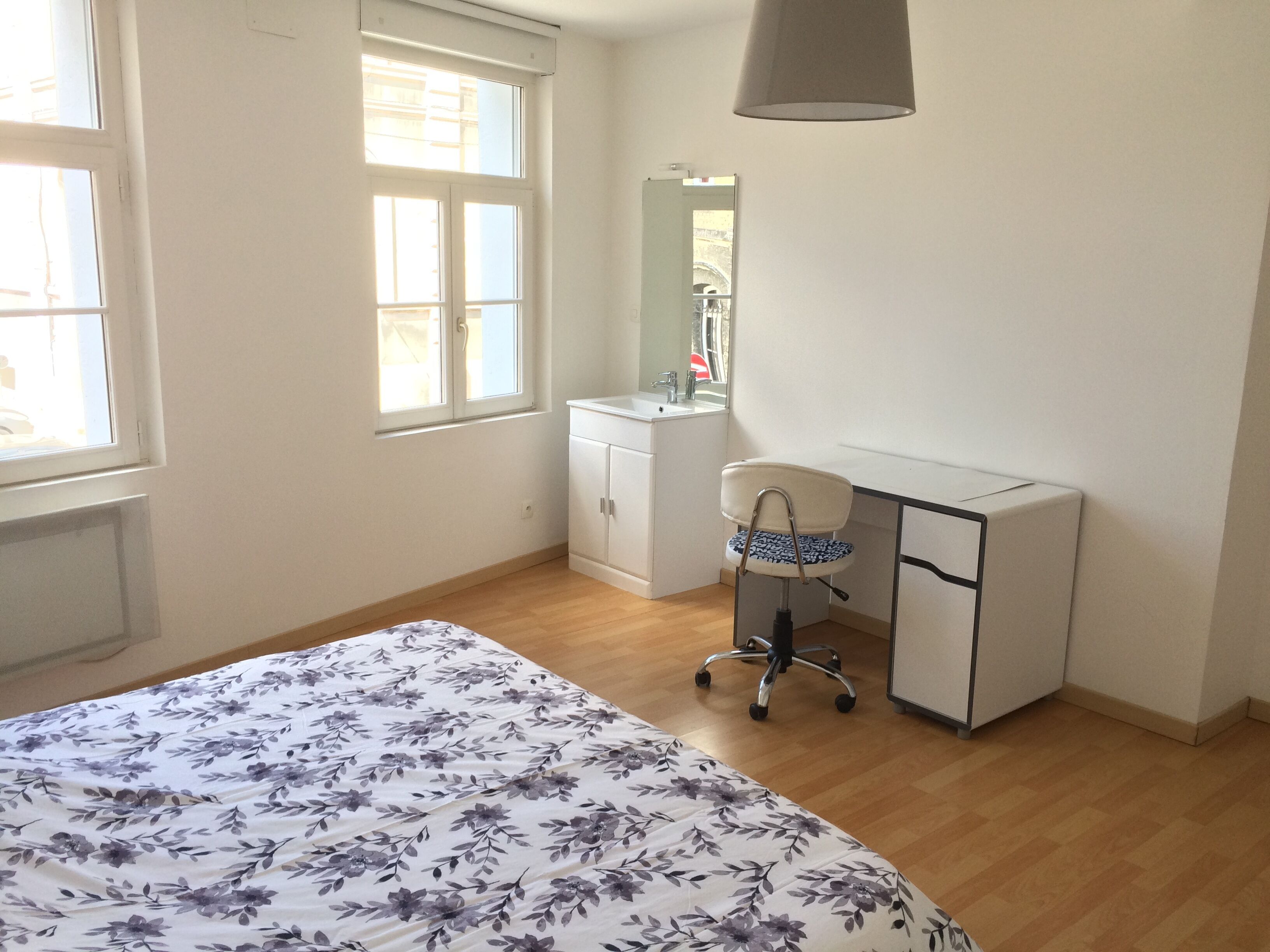 Une chambre à coucher avec un lit, un bureau, une chaise, une fenêtre et un miroir.