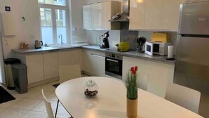 Eine moderne Küche mit weißen Schränken, einem Edelstahlkühlschrank, einer Mikrowelle und einem Spülbecken. Ein Esstisch mit Stühlen und eine Vase mit roten Blumen stehen bereit.