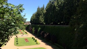 Ein formaler Garten mit ordentlich geschnittenen Hecken, einer zentralen runden Fontäne und einer symmetrischen Gestaltung.