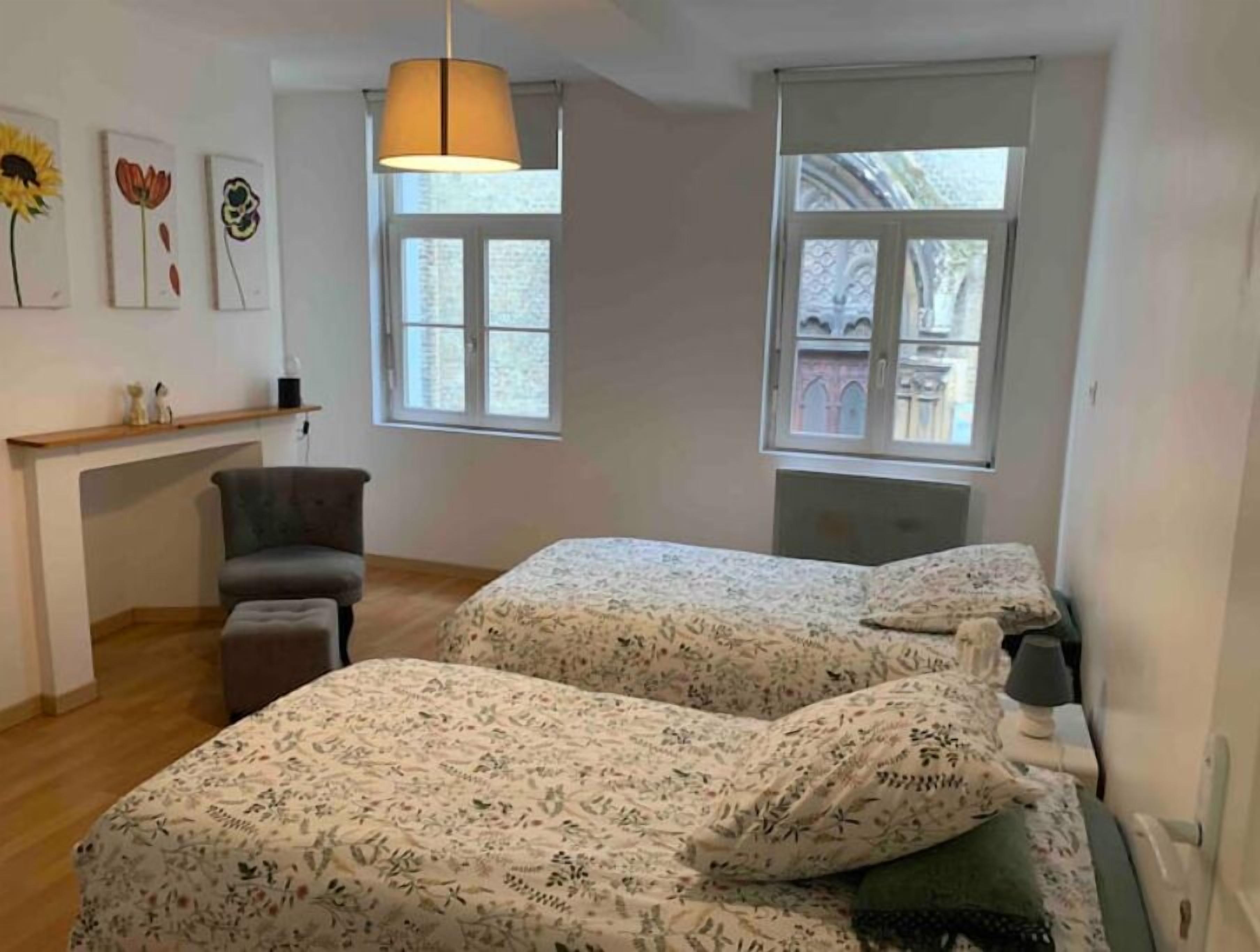 Een slaapkamer met twee bedden, een stoel, een bureau en een raam.