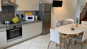 Eine moderne Küche mit Einbauofen, Mikrowelle und Kühlschrank. Es gibt einen Esstisch mit Stühlen und eine kleine Pflanze auf der Arbeitsfläche.