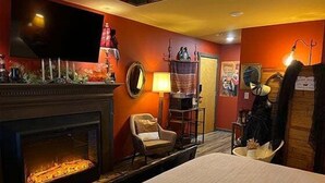 A hotel room with a fireplace, a television, a chair, and a bed. - Empty Arms Parlor - Rm. 208 (Stanardsville)